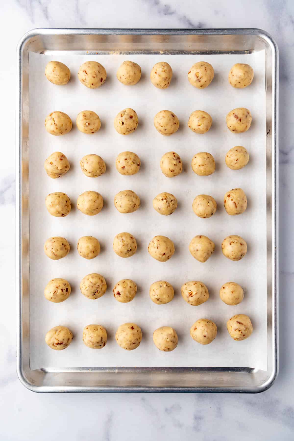 An overhead image of a baking sheet lined with parchment paper with rows of cookie dough on it.