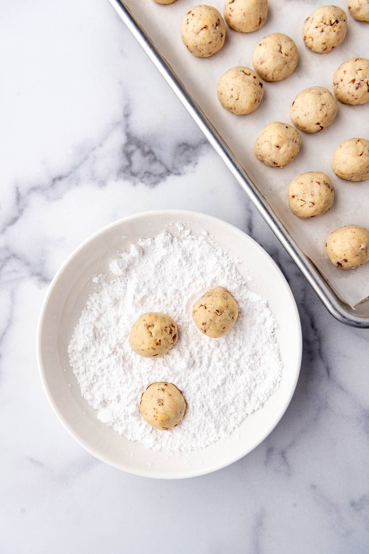 Rolling baked cookies in a bowl of powdered sugar.