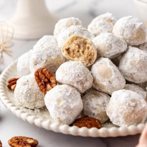 A pile of Mexican wedding cookies and pecans with one cookie bitten to reveal insides.