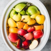 a slow cooker with fresh fruit and cinnamon and cloves inside