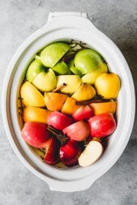 a slow cooker with fresh fruit and cinnamon and cloves inside