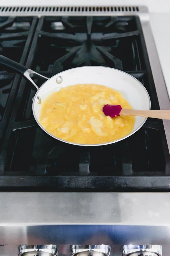 An image of partially scrambled eggs on the stovetop where curds are starting to form.
