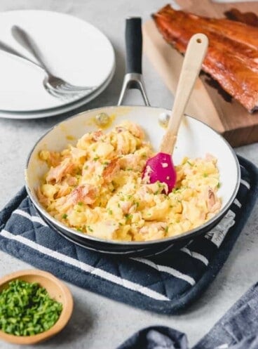 smoked salmon scrambled eggs in a skillet with a bowl of chives and smoke salmon fillet to the sides