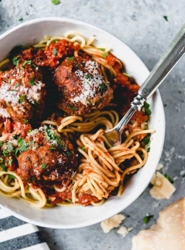 a white bowl with spaghetti and meatballs with a fork twirled in noodles