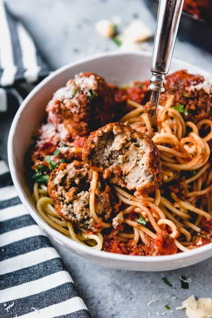 An image of meatballs and spaghetti with a bite taken out of one of the meatballs in the rich tomato sauce.