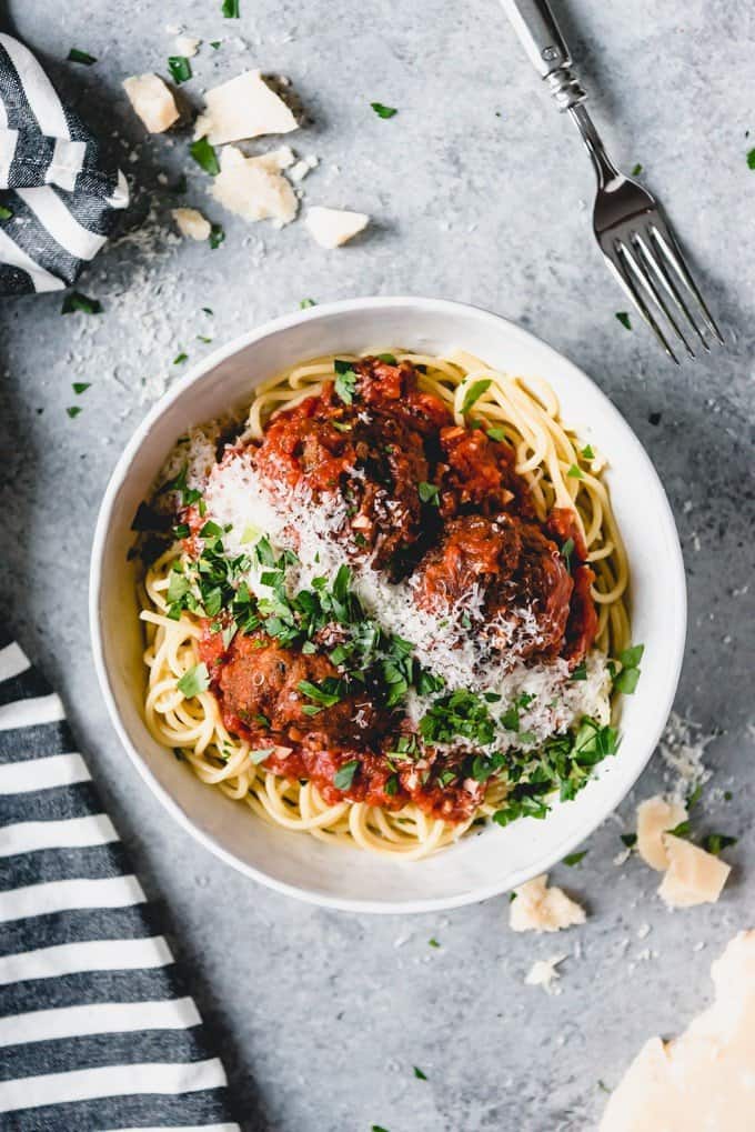 An image of a big bowl of Italian meatballs and spaghetti sprinkled with freshly chopped parsley and grated Parmesan cheese.