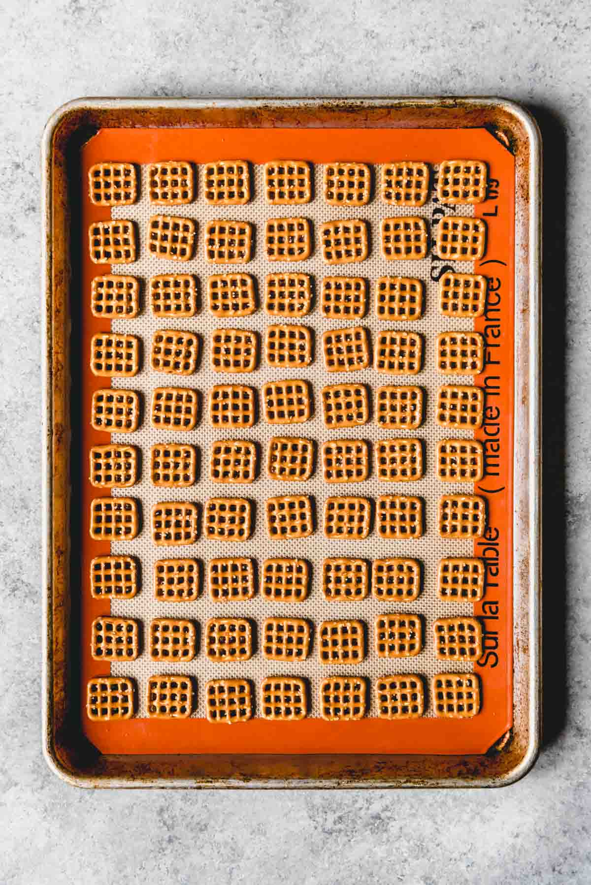 An image of square pretzels arranged in rows on a baking sheet.