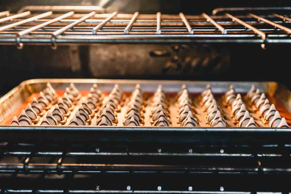 An image of pretzels and Hershey's hugs on a baking sheet in the oven, melting to make easy Christmas pretzels treats.