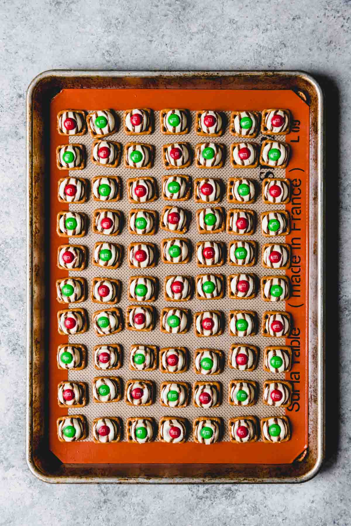 An image of red and green M&M's pressed into Hershey's Hugs on pretzels on a baking sheet.