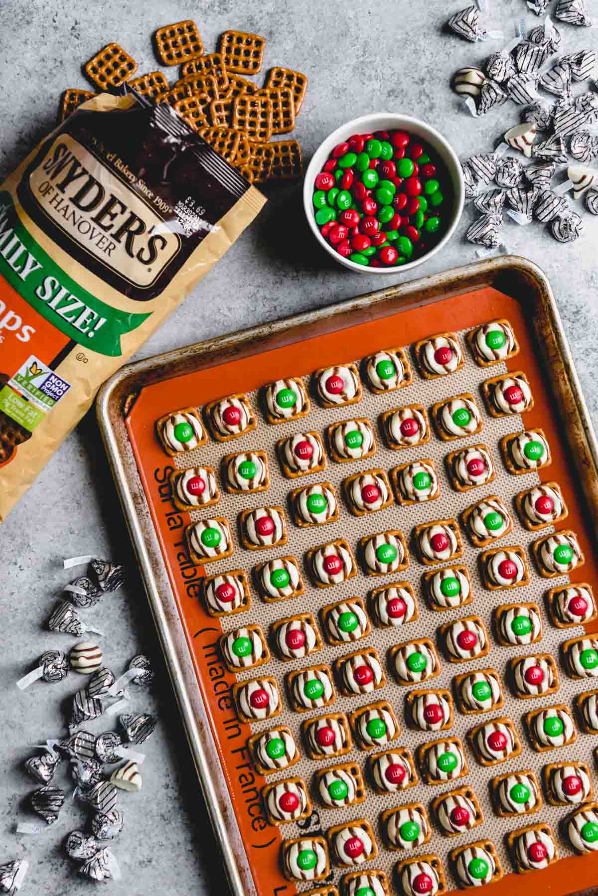 An image of Christmas hugs made with square pretzel snaps, melted Hershey's hugs, and red and green Christmas M&M's.