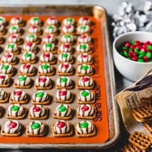 An image of easy pretzel hugs with red and green Christmas M&M's on a baking sheet with a silpat mat.