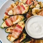 an aerial view of Bacon Wrapped Jalapeno Poppers and a bowl of dip on a white plate.