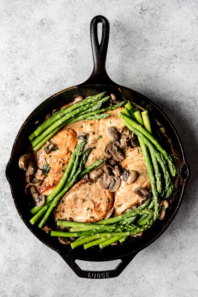 An image of chicken, mushrooms, asparagus, and a Madeira cream sauce in a cast iron skillet for Chicken Madeira made at home.