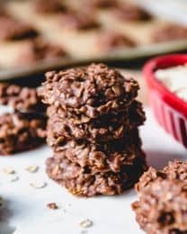 stacked no bake cookies with a baking tray full of more in the background