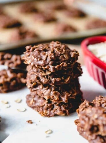 stacked no bake cookies with a baking tray full of more in the background