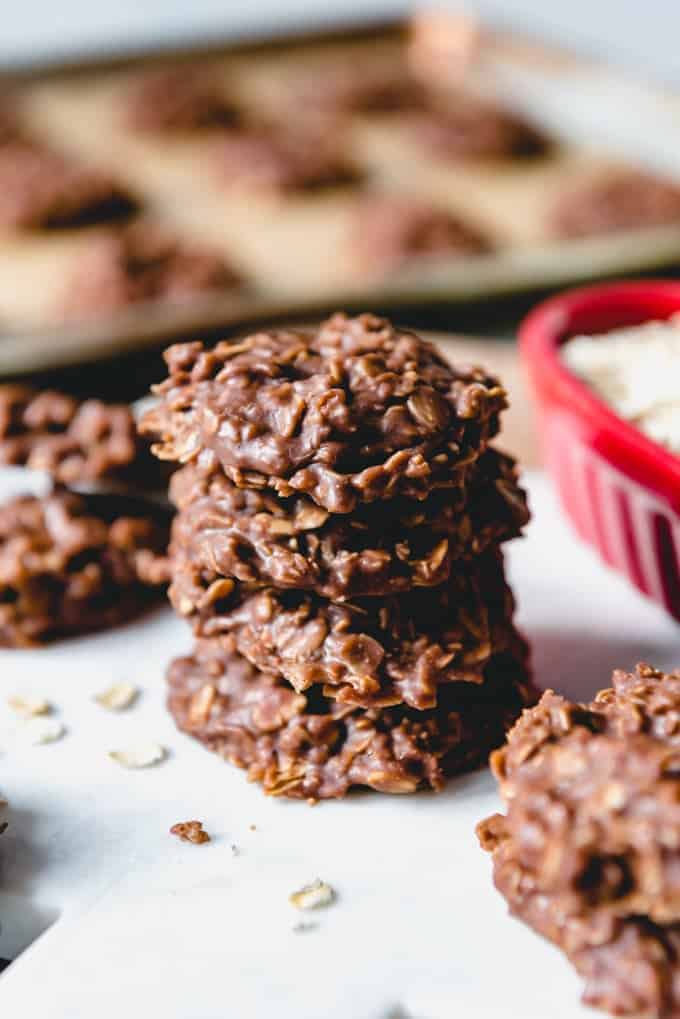 stacked no bake cookies with a baking tray full of more in the background