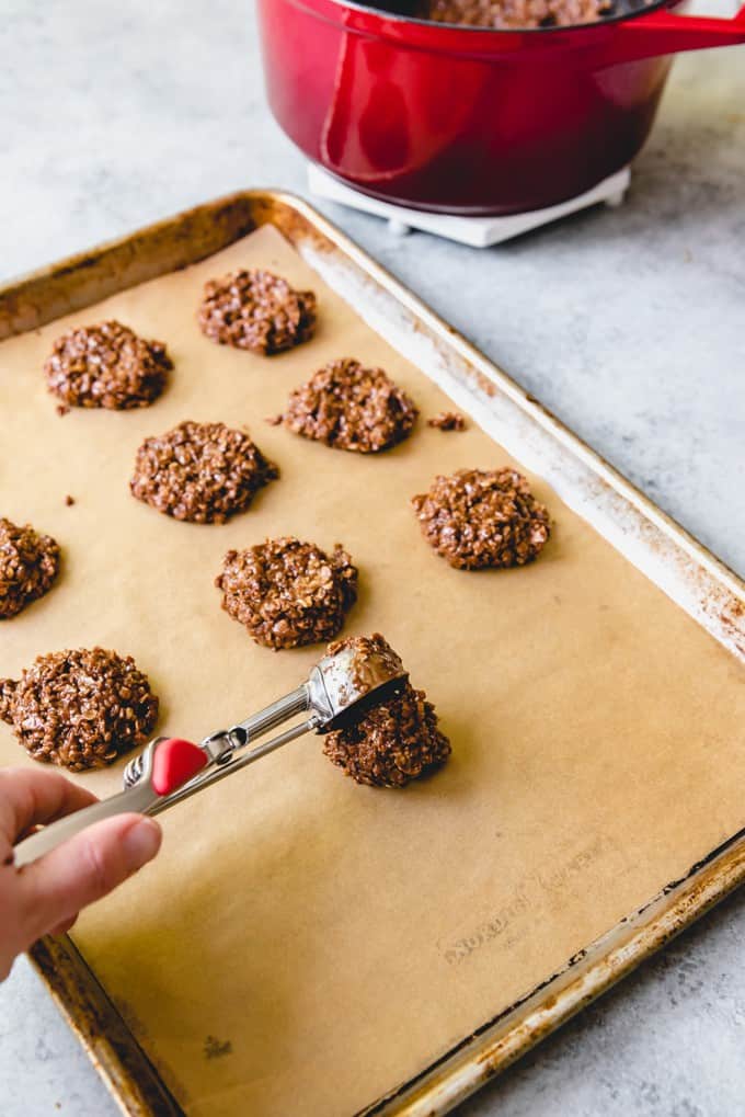 An image of a cookie scoop dropping no bake cookie mixture onto a parchment-lined baking sheet.