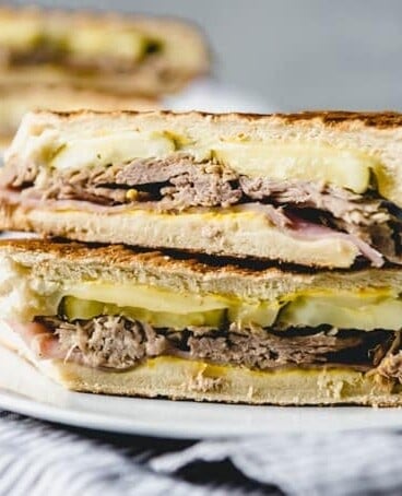 a sliced and stacked cubanos sandwich on a white plate