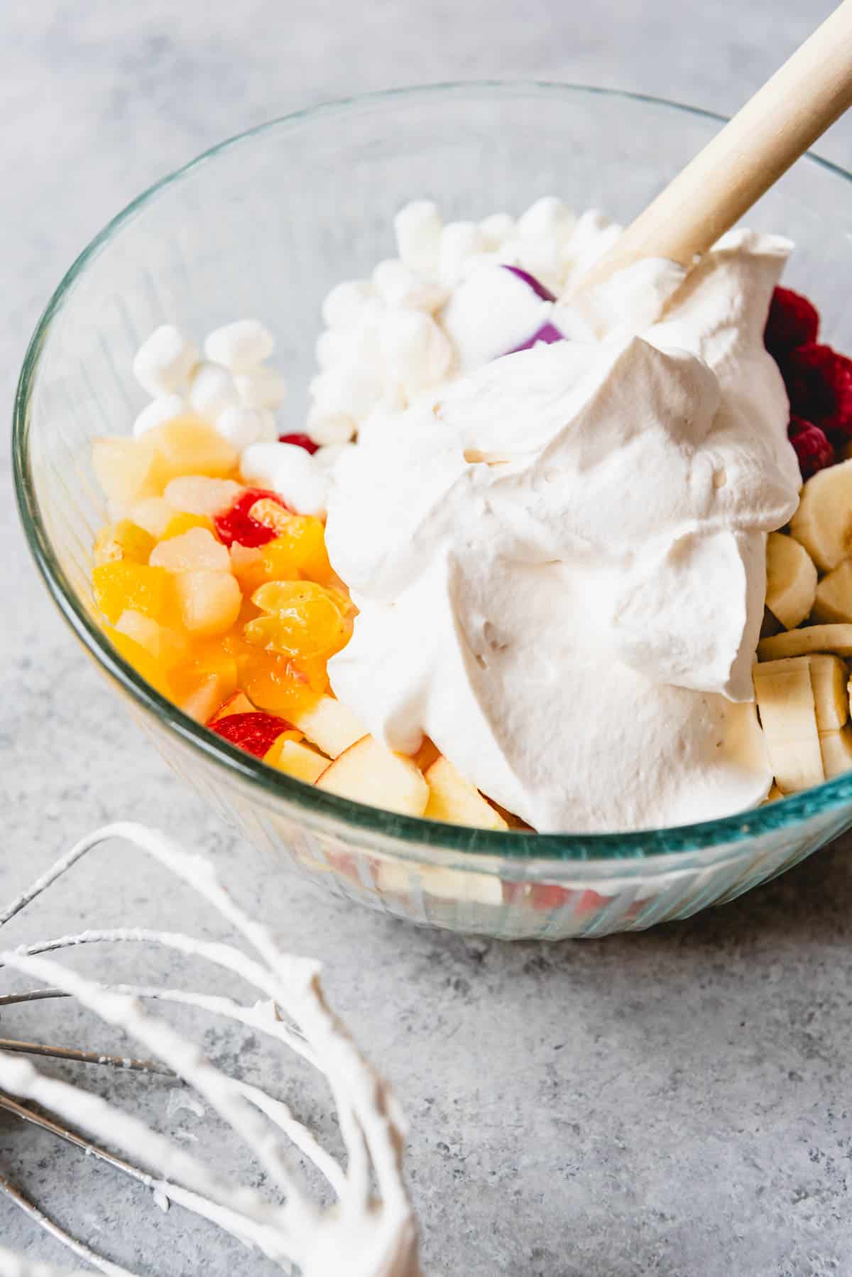 An image of a bowl of fruit cocktail with whipped cream, fresh fruit, and marshmallows for making an easy fruit salad.