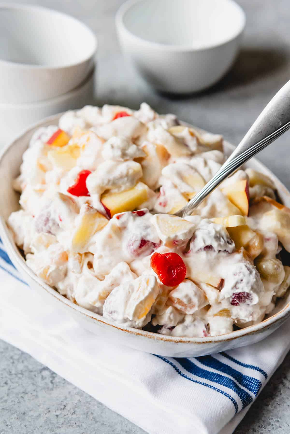 A bowl filled with fruit salad with marshmallows and whipped cream.
