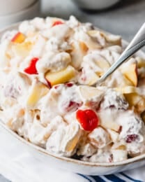 A bowl filled with fruit salad with marshmallows and whipped cream.