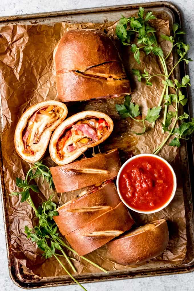 peppers and sausage inside a sliced stromboli on a baking sheet with herbs and sauce