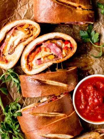 sliced sausage and pepper stromboli on a parchment paper lined baking sheet with a bowl of sauce to the side