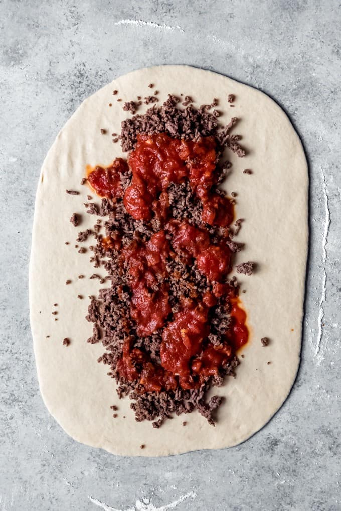 ground beef and red sauce down the middle of a rolled out flat piece of dough