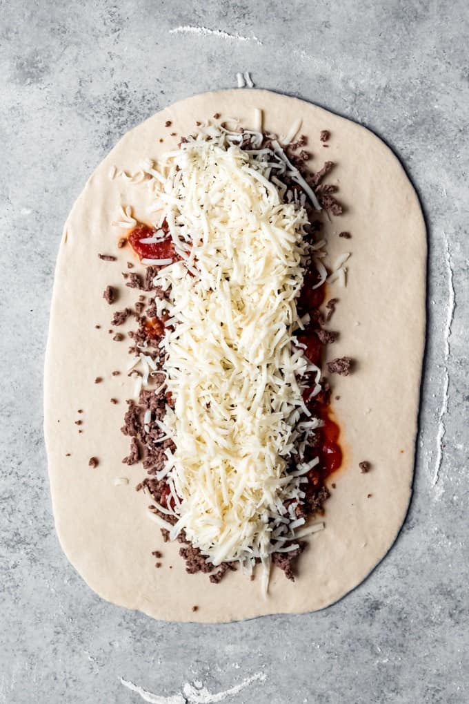a thin rolled piece of dough topped with cooked ground beef, sauce, and cheese