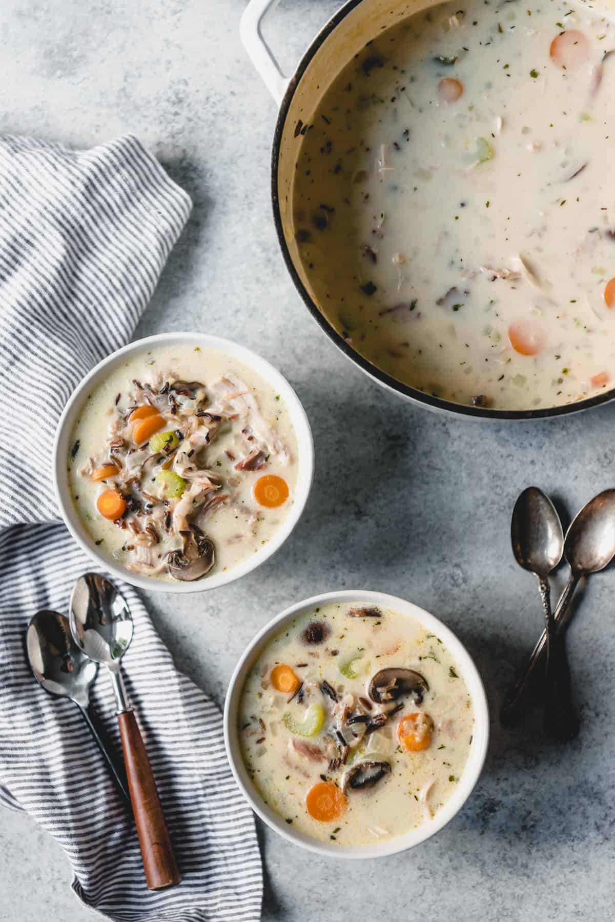 Two bowls of creamy turkey soup with wild rice next to a large pot of the soup.