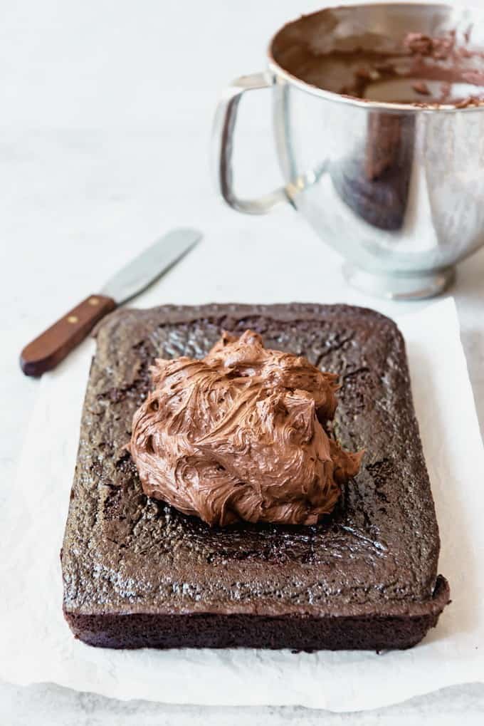 An image of a single layer of moist chocolate cake with a pile of chocolate buttercream on top ready to be spread out to frost the cake.