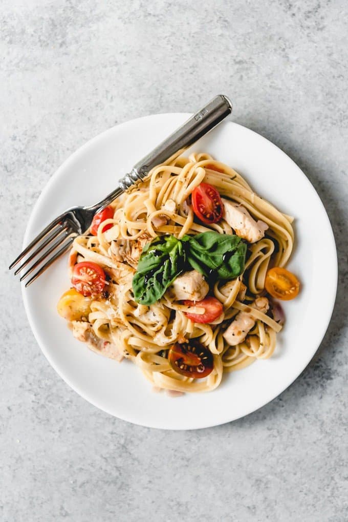 An image of a plate of linguine pasta with tomatoes, chicken, basil, and a Parmesan on a white plate.