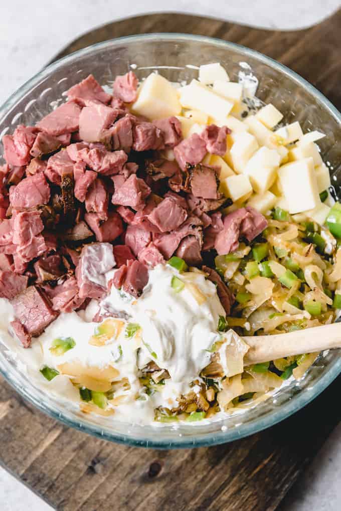 An image of the ingredients for Philly Cheese Steak Dip being stirred together in a bowl to combine.