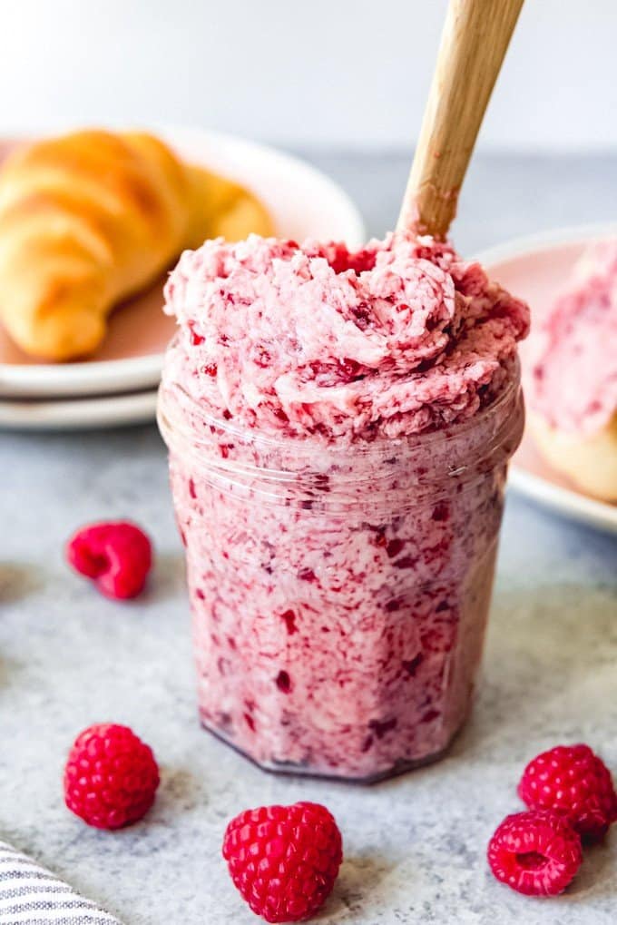 An image of a jar filled with homemade raspberry butter with fresh raspberries around it.