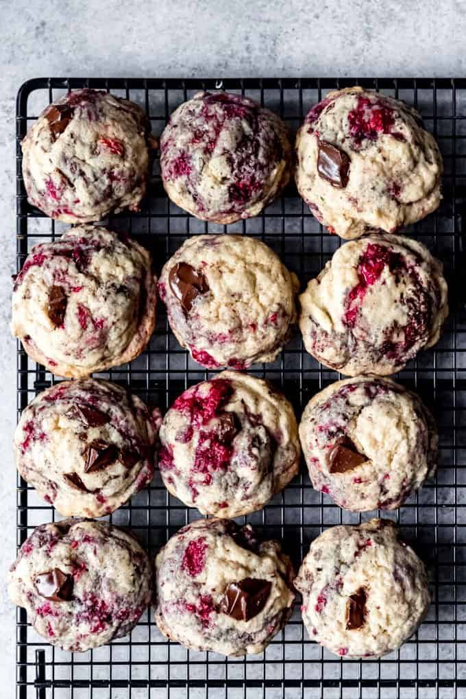An image of dark chocolate chunk cookies with raspberries cooling on a wire cooling rack.