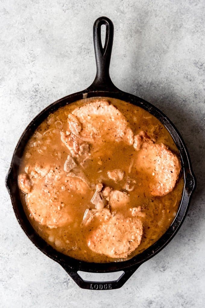 An image of pork chops in an onion gravy in a large cast iron skillet.