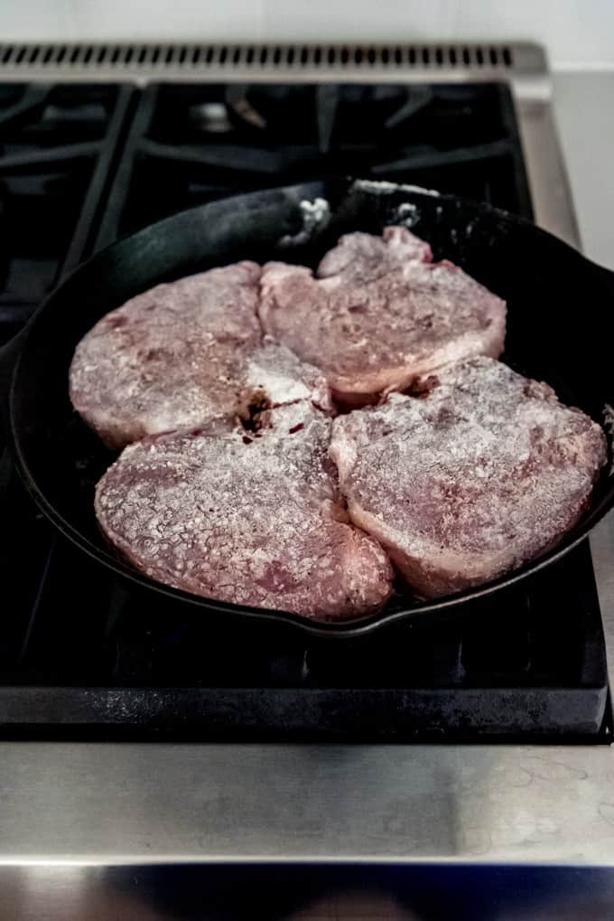 An image of 4 bone-in pork chops in a cast iron skillet.