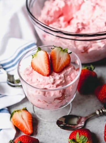 creamy strawberry cottage cheese jello in a cup and in a bowl with fresh strawberries