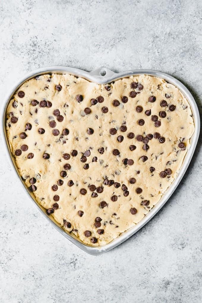 An image of chocolate chip cookie dough pressed into a heart-shaped giant cookie pan.
