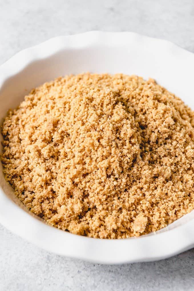 An image of buttery graham cracker crumbs ready to be pressed into a white pie plate to make a graham cracker crust from scratch.