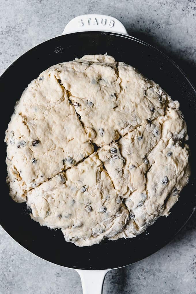 An image of an unbaked loaf of Irish soda bread in a cast iron pan with a cross sliced into the top to help it bake more evenly.
