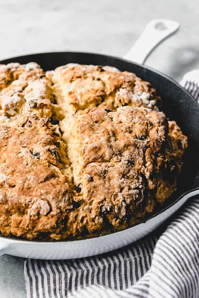 An image of Irish soda bread with currants baked in a cast iron pan with a cross sliced into the top.