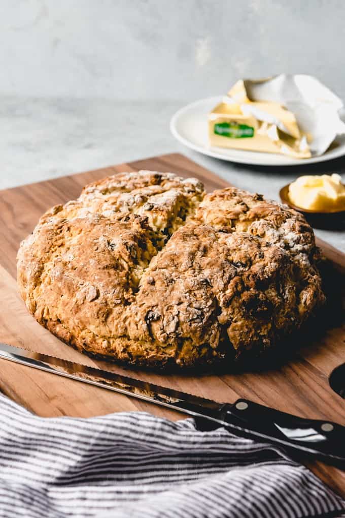 An image of a loaf of homemade Irish soda bread cooling on a cutting board that is ready to be sliced with a knife and spread with butter.