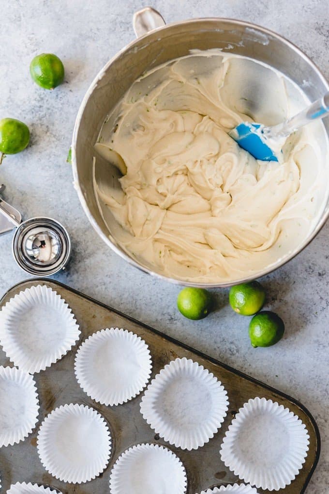 An image of key lime cake batter next to a muffin tin lined with white cupcake liners.