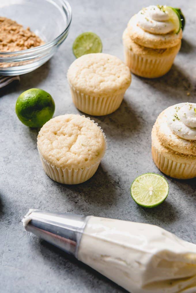 An image of unfrosted cupcakes with a piping bag filled with key lime buttercream frosting for decorating the cupcakes.