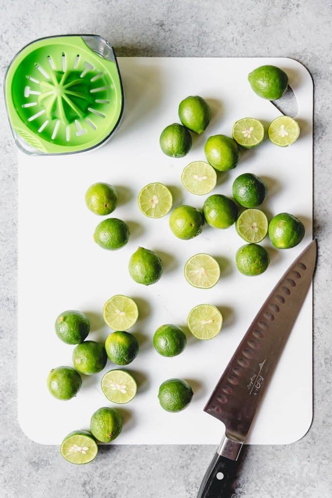 An image of key limes on a cutting board next to a juicer.