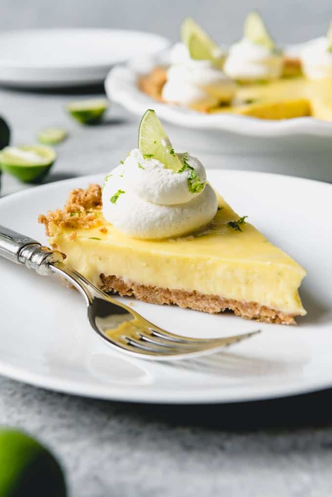 An image of a slice of key lime pie with whipped cream on a white plate with a fork.