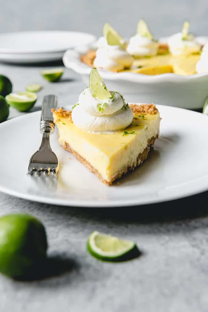 An image of a slice of classic key lime pie topped with whipped cream and key lime zest on a graham cracker crust.