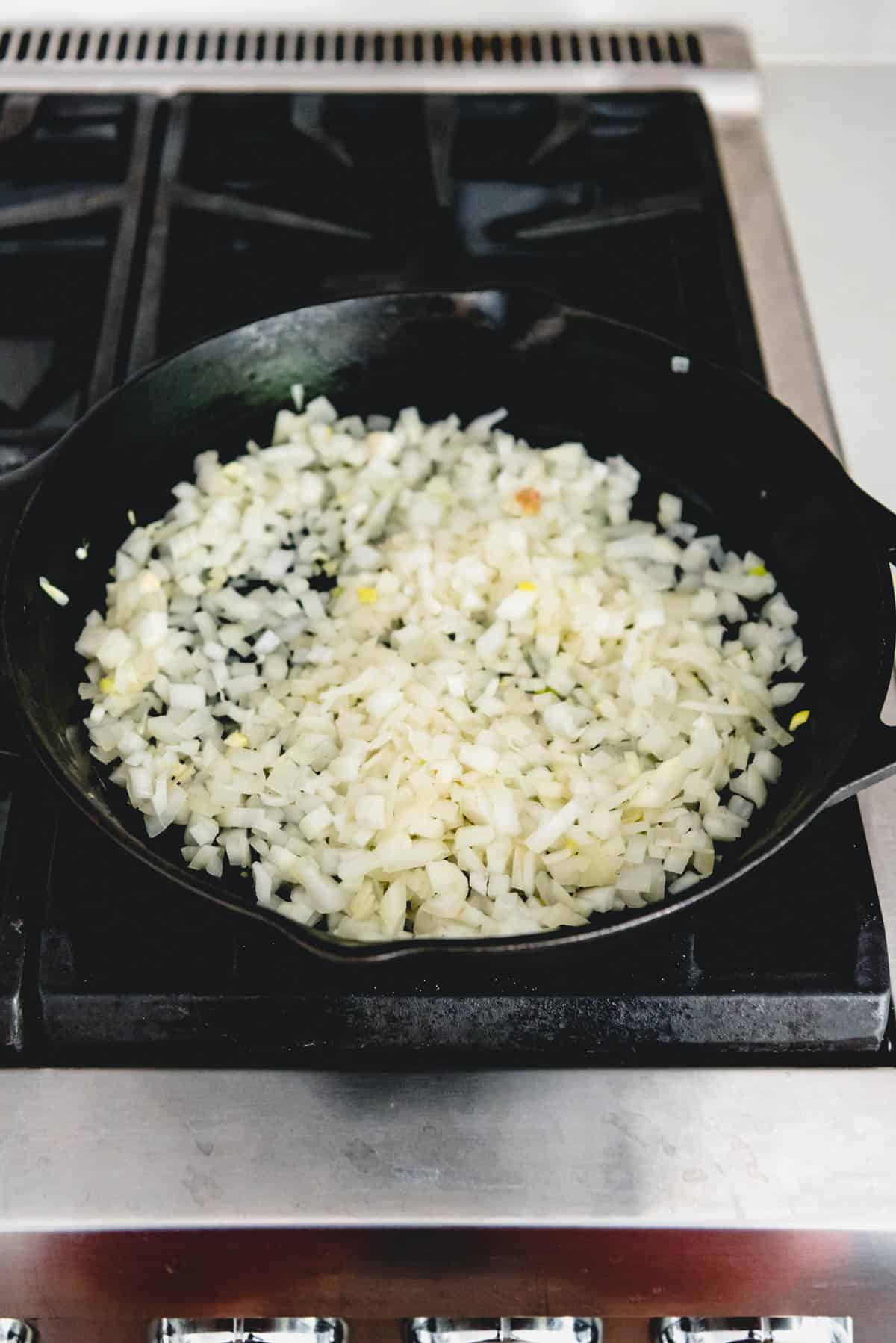 Sauteeing diced onions in a cast iron skillet on the stovetop.