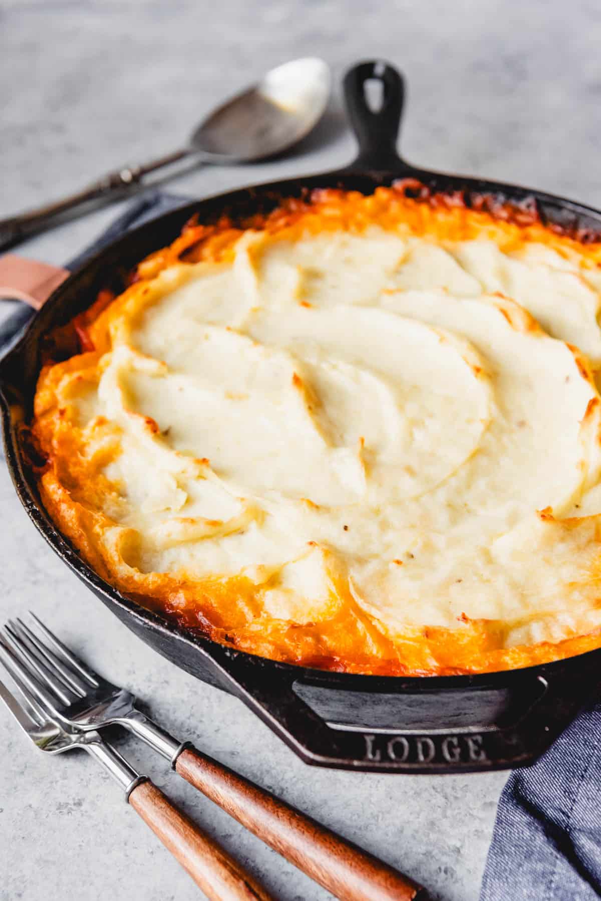 An image of a baked shepherd's pie in a cast in pan ready for serving with creamy swirls of golden brown mashed potatoes on top.